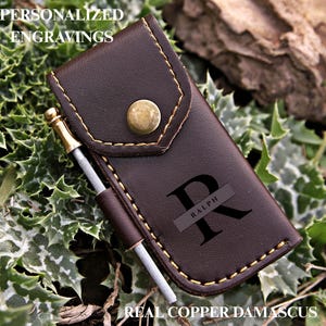 May include: A dark brown leather case with a brass snap closure and a side loop holding a metal tool. The case features the engraved letter R with the name RALPH inside it. Text on the image reads PERSONALIZED ENGRAVINGS and REAL COPPER DAMASCUS.