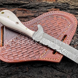 handmade damascus bull cutter knife with white handle and pancake leather sheath, the knife handle is assembled with brass pins and has a mosaic pin in the center, the damascus pattern and the file work on the spine of knife truly speaks about how well crafted this knife is