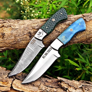 May include: Two knives with fixed blades. The top knife features a dark green handle with a honeycomb pattern and a Damascus steel blade engraved with SB. The bottom knife has a blue handle and a smooth steel blade engraved with 01/08/2023.