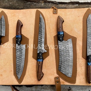 May include: Set of five kitchen knives with wooden handles and a blue accent. The knives are arranged in a leather roll with individual slots for each knife. The knives have a Damascus steel pattern.