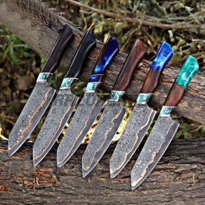 May include: Six handcrafted chef knives with patterned blades and wooden handles. The handles feature various colors, including dark brown, black, and blue, with decorative accents. The blades have a copper-colored edge.
