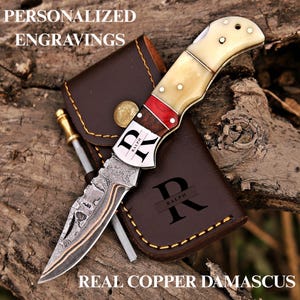 May include: A folding pocket knife with a Damascus steel blade featuring copper accents, a handle with cream, red, and dark wood segments, and a metal bolster engraved with the name RALPH. Includes a brown leather sheath with the letter R.