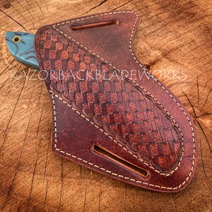 May include: A brown leather knife sheath with a woven pattern and light brown stitching detail. The sheath is designed to hold a knife with a blue and black handle.