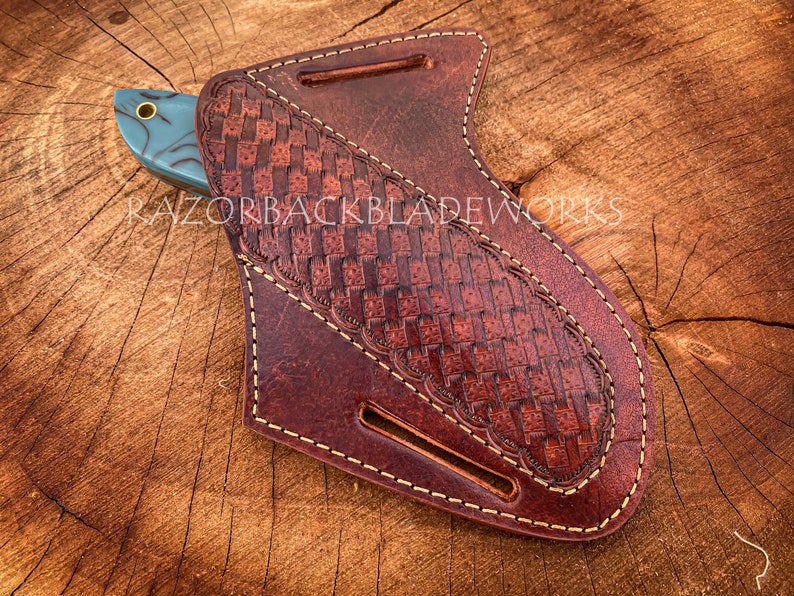 May include: A brown leather knife sheath with a woven pattern and light brown stitching detail. The sheath is designed to hold a knife with a blue and black handle.