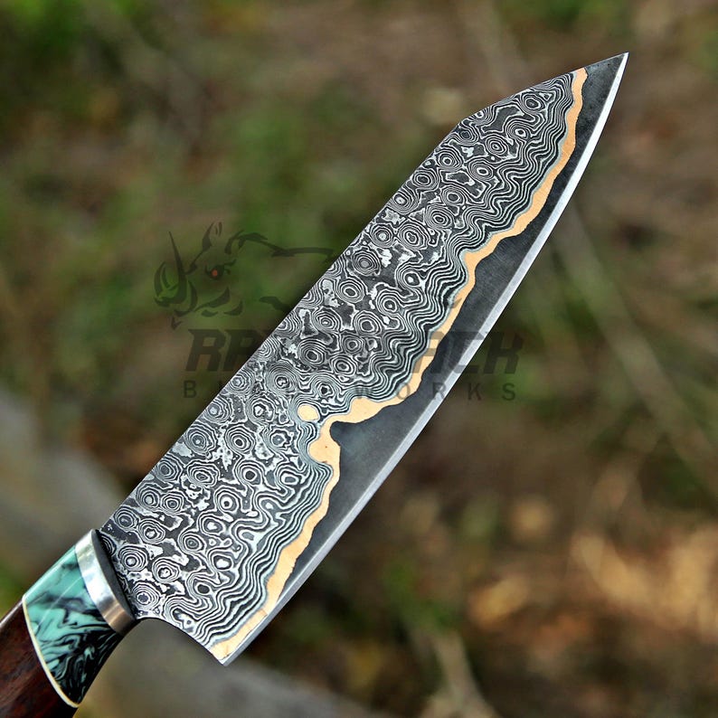 May include: A chef knife featuring a complex Damascus steel blade with a wavy, layered pattern in black, gray, and copper tones. The handle is crafted from dark wood with a marbled teal and black resin bolster, finished with a silver metal ferrule.