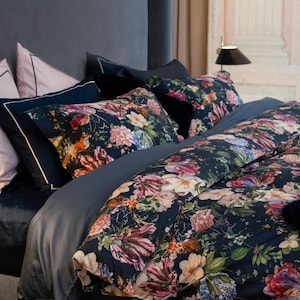 Könnte beinhalten: Ein Bett mit dunkelblauem Kopfteil und Bettwäsche. Die Bettwäsche umfasst dunkelblaue Kissen mit weißem Rand sowie Kissen und Bettbezug mit Blumendruck. Das Blumenmuster zeigt rosa, orange und weiße Blumen auf dunklem Hintergrund.