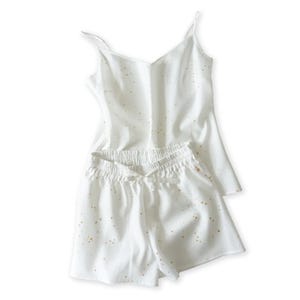 Puede incluir: Conjunto de pijama blanco con top de tirantes y shorts. El conjunto presenta un delicado estampado de salpicaduras doradas. El top tiene tirantes finos y cuello en V. Los shorts tienen cintura elástica con cordón.