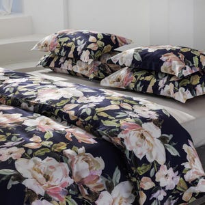 May include: A navy blue floral bedding set featuring large, light pink and white flowers with green leaves. The set includes a duvet cover and several pillowcases. The bedding is arranged on a bed, with the pillowcases stacked on top.