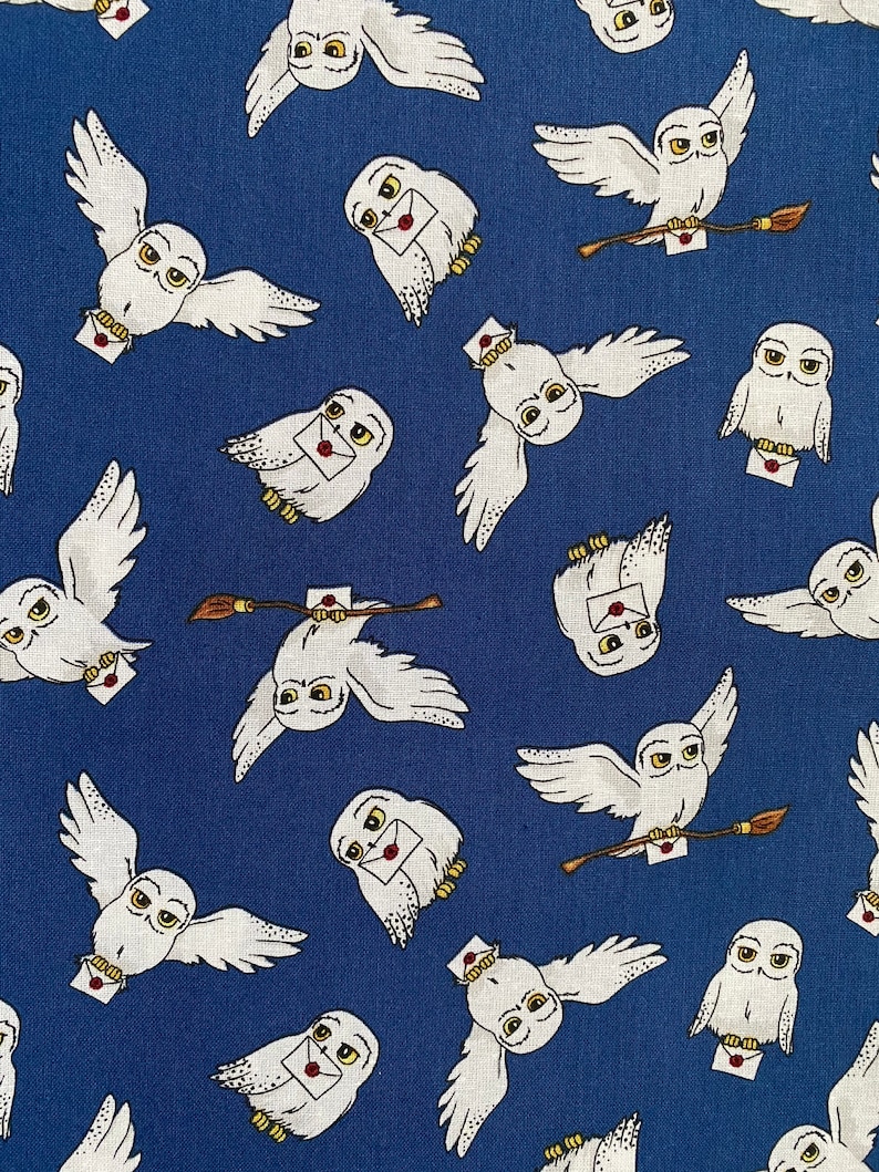 May include: A blue fabric with a repeating pattern of white owls carrying letters and a brown twig. The owls have yellow eyes and are flying.
