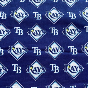 May include: A blue fabric with a repeating pattern of white diamond shapes. Each diamond has the words "Rays" and "TB" in white text.