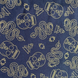 May include: A navy blue fabric with a repeating pattern of gold skulls, snakes, and geometric shapes. The skulls have a heart in the center of their foreheads.