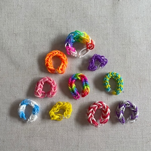 May include: A collection of ten colorful rubber band bracelets in various patterns, including rainbow, pink, yellow, blue, and purple.