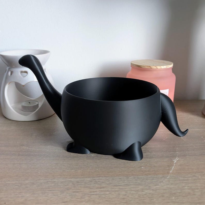 May include: A black ceramic planter shaped like a dinosaur with a long neck and tail. The planter has a round body and four small legs.