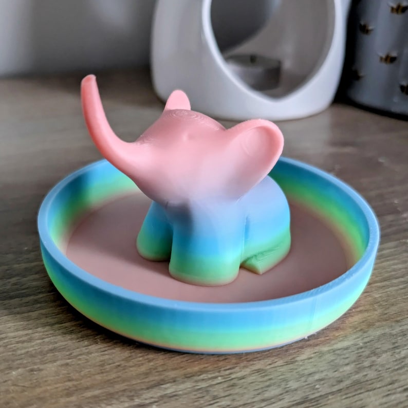 May include: A rainbow ombre ceramic trinket dish with a small pink, blue, and green elephant figurine in the center.