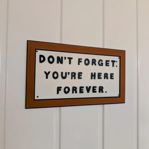 May include: A brown wooden sign with white lettering that reads "Don't forget: You're here forever."