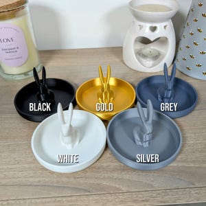 May include: Five ring dishes in different colours: black, gold, grey, white, and silver. Each dish features a small rabbit figurine.
