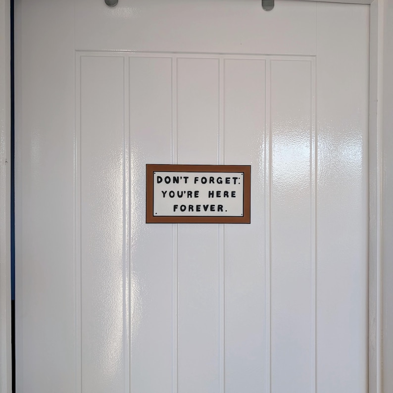 May include: A white door with a brown sign that reads "Don't forget: You're here forever."