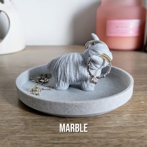 May include: A light gray marble tray with a Highland cow figurine. The cow holds rings on its horns. A silver necklace rests on the tray. The word "MARBLE" is printed in white at the bottom.
