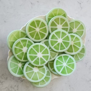 May include: A white plate filled with green lime-shaped soaps. The soaps are arranged in a circular pattern and have a white center.