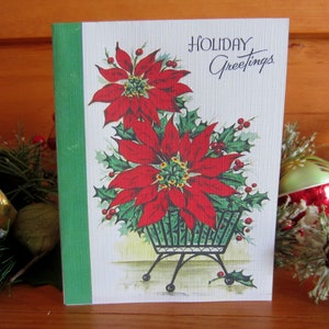 May include: A vintage Christmas card featuring a red poinsettia plant in a black metal planter. The card has a green border and the text "HOLIDAY Greetings" in black script.