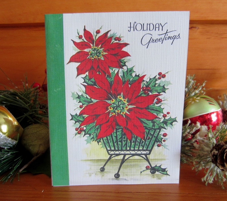 May include: A vintage Christmas card featuring a red poinsettia plant in a black metal planter. The card has a green border and the text "HOLIDAY Greetings" in black script.