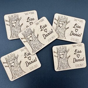 May include: A collection of five square, light brown wedding favors. Each features a tree with a heart carved into it, the names "Lisa" and "Daniel", and the date "12.03.2023". The words "Save the Date" are also included.