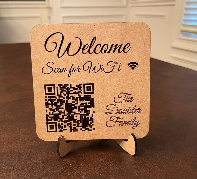 A light brown wooden sign with "Welcome Scan for WiFi" and a WiFi symbol at the top, a QR code in the middle, and "The Doubler Family" at the bottom, all in dark brown text.
