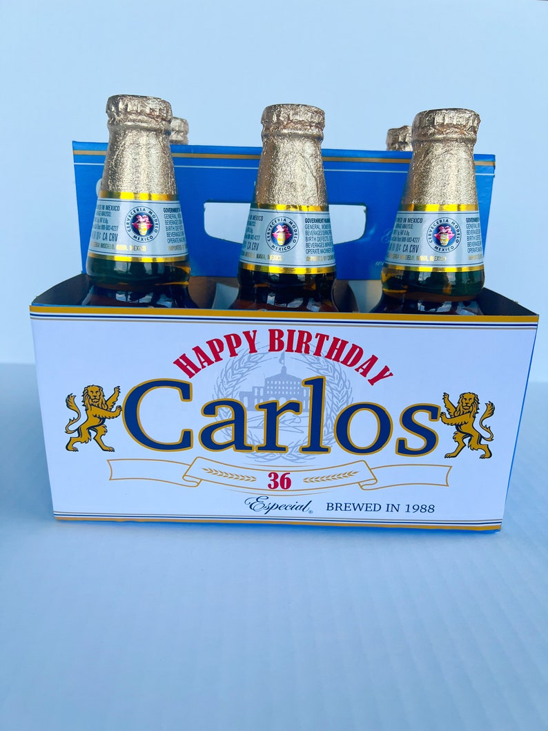 May include: A six-pack of beer with a blue and white cardboard carrier. The carrier has a gold lion on each side and says "Happy Birthday Carlos 36 Especial Brewed in 1988".