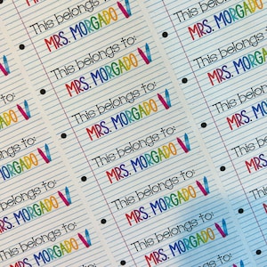 Pu&ograve; includere: Un foglio di etichette per nomi personalizzate e colorate con il testo "This belongs to: MRS. MORGADO" e un'illustrazione di pastelli colorati.