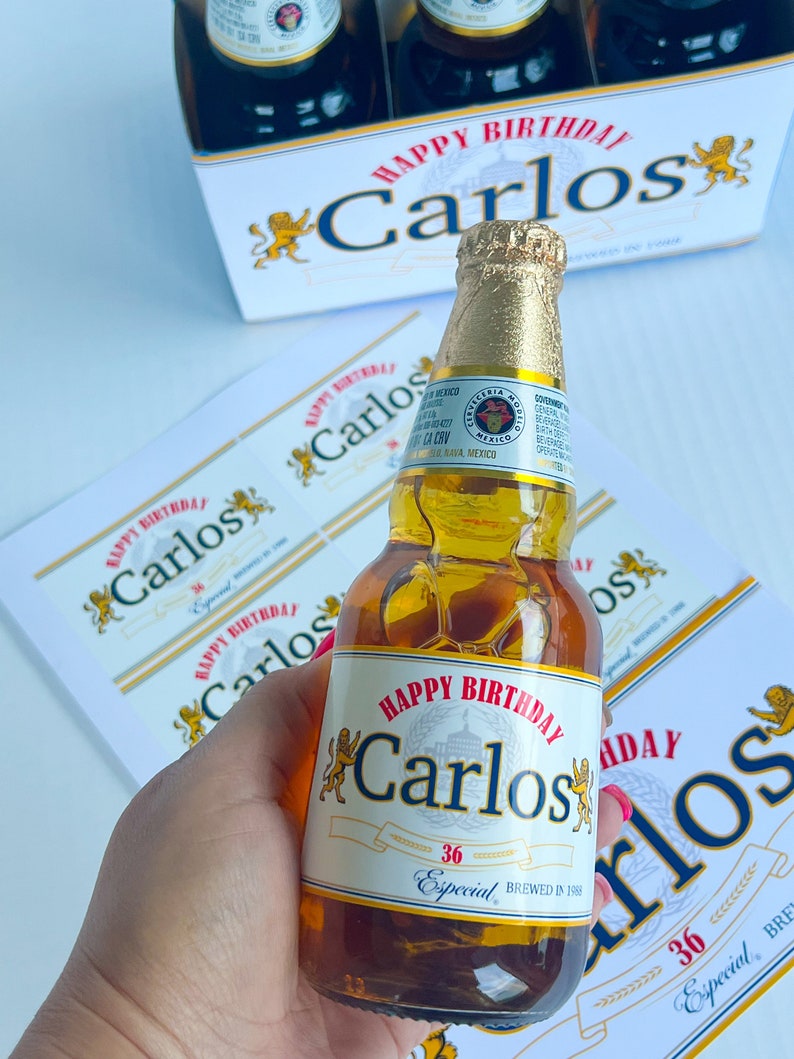 May include: A personalised beer bottle with a white label that says "Happy Birthday Carlos" with a lion graphic on either side of the text. The label also says "36 Especial Brewed in 1988".