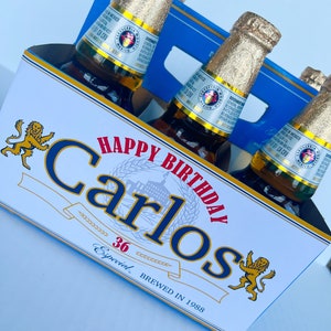 May include: A six-pack of beer with a personalised label that says "Happy Birthday Carlos 36 Especial Brewed in 1988". The label features a lion graphic and a blue and red colour scheme.
