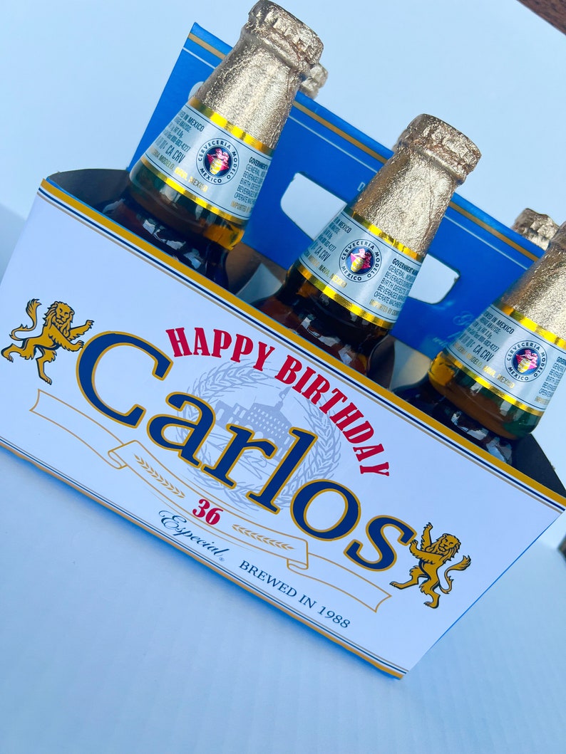 May include: A six-pack of beer with a personalised label that says "Happy Birthday Carlos 36 Especial Brewed in 1988". The label features a lion graphic and a blue and red colour scheme.