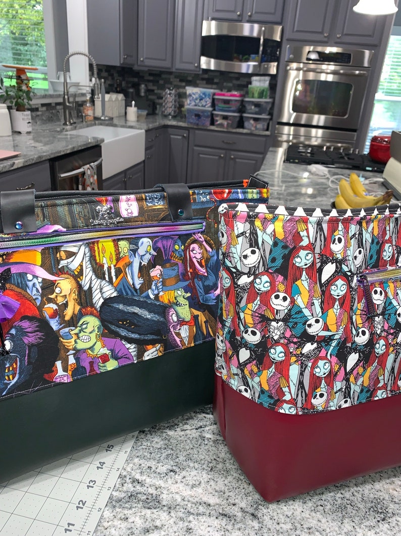 May include: Two tote bags with a green and red base and a colorful print of characters from the Nightmare Before Christmas movie. The bags have a zipper and a top handle.