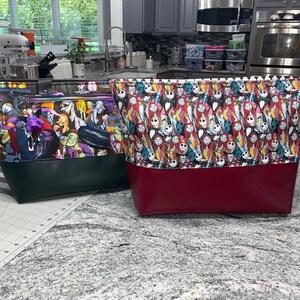 May include: Two large tote bags with colorful fabric designs. The bag on the left has a green and black design with a scene of characters from a movie. The bag on the right has a red and black design with a pattern of faces from a movie. Both bags have a solid colored bottom.