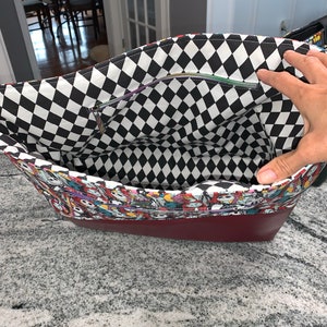 May include: A red and black checkered fabric tote bag with a zippered pocket. The bag is lined with a colorful fabric featuring characters from the Nightmare Before Christmas.