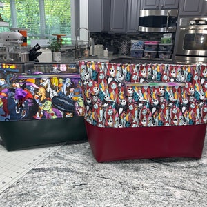 May include: Two tote bags with a Nightmare Before Christmas theme. One bag is green with a black bottom and features characters from the movie. The other bag is red with a black bottom and features Jack Skellington and Sally.