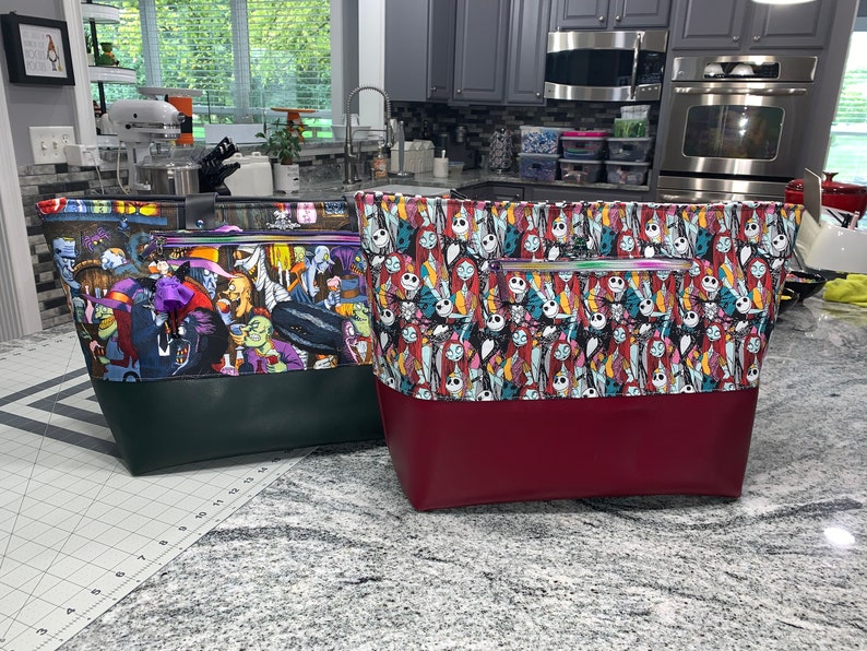 May include: Two tote bags with a Nightmare Before Christmas theme. One bag is green with a black bottom and features characters from the movie. The other bag is red with a black bottom and features Jack Skellington and Sally.