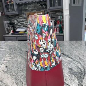 May include: A red tote bag with a colorful print of characters from The Nightmare Before Christmas. The print features Jack Skellington, Sally, and other characters from the film.