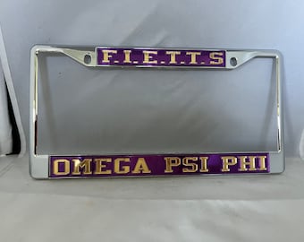 Könnte beinhalten: Ein silberner Nummernschildrahmen mit einer violetten und goldenen Aufschrift, die "F.I.E.T.T.S. OMEGA PSI PHI" lautet.