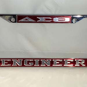May include: A silver license plate frame with a red background and the letters "ΔΣΘ" and the word "ENGINEER" in silver lettering.