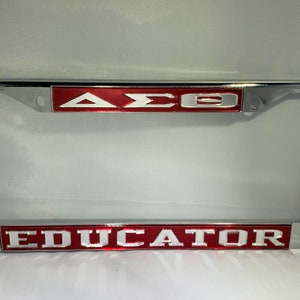 May include: Chrome license plate frame with a red background and white letters. The top of the frame says "ΔΣΘ" and the bottom says "EDUCATOR".