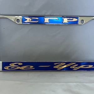 May include: A chrome license plate frame with a blue and gold design. The top of the frame has the letters "EGP" in gold lettering on a blue background. The bottom of the frame has the words "Ee-Yip" in gold lettering on a blue background.