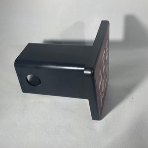 Puede incluir: Un receptor de enganche de metal negro con una abertura cuadrada y un agujero redondo. El receptor tiene una placa de color burdeos unida a &eacute;l con el texto "ALB 193" en letras plateadas.