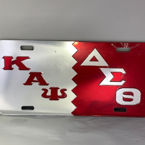 May include: A silver and red metal license plate with the Greek letters "ΚΑΨ" on the silver side and "ΔΣΘ" on the red side.