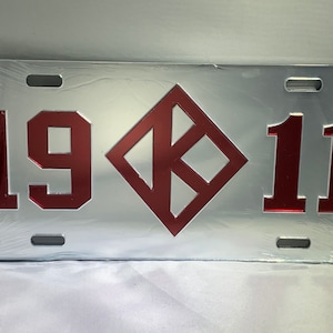 May include: A silver metal license plate with the numbers 1911 and a red diamond-shaped logo in the center.