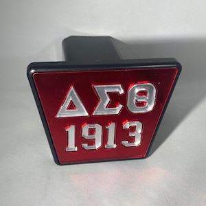 Puede incluir: Una tapa de enganche roja y plateada con las letras "&Delta;&Sigma;&Theta;" y el n&uacute;mero "1913" en ella.