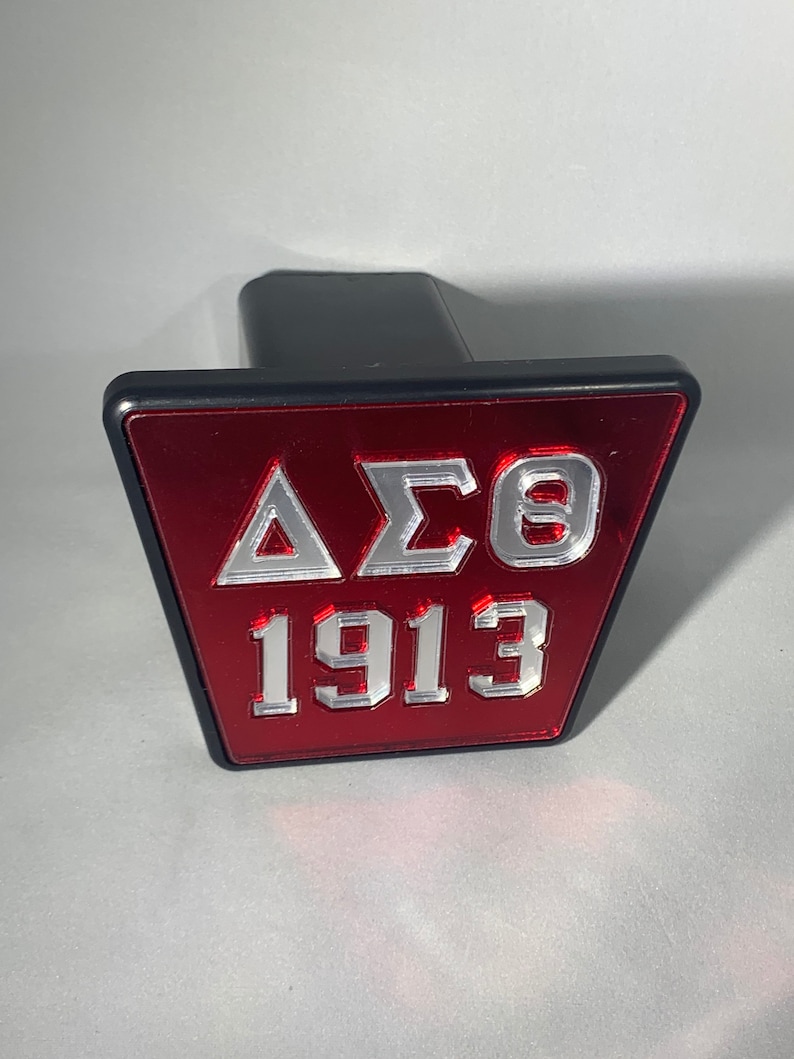 Puede incluir: Una tapa de enganche roja y plateada con las letras "&Delta;&Sigma;&Theta;" y el n&uacute;mero "1913" en ella.