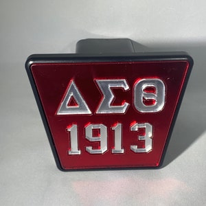 Puede incluir: Una cubierta de enganche triangular roja y negra con las letras "&Delta;&Sigma;&Theta;" y el n&uacute;mero "1913" en letras plateadas.