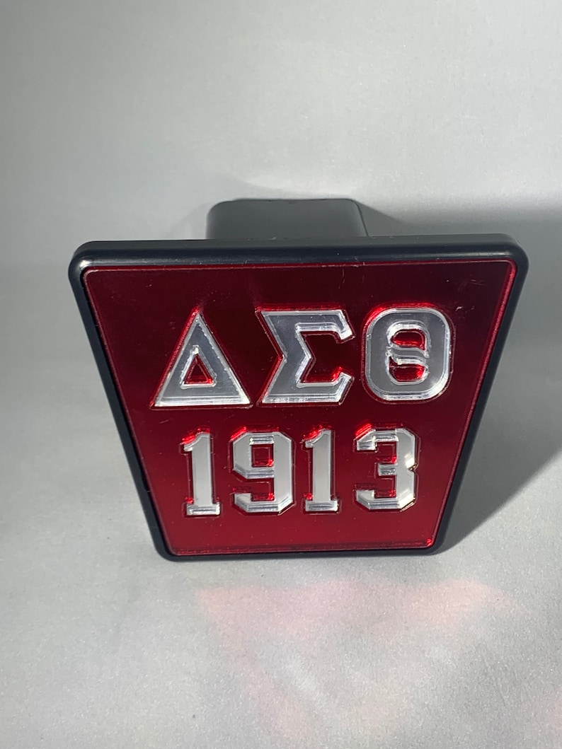 Puede incluir: Una cubierta de enganche triangular roja y negra con las letras "&Delta;&Sigma;&Theta;" y el n&uacute;mero "1913" en letras plateadas.