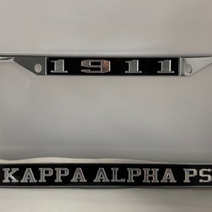 May include: Chrome license plate frame with black background and silver lettering. The frame says "1911" and "Kappa Alpha Psi".
